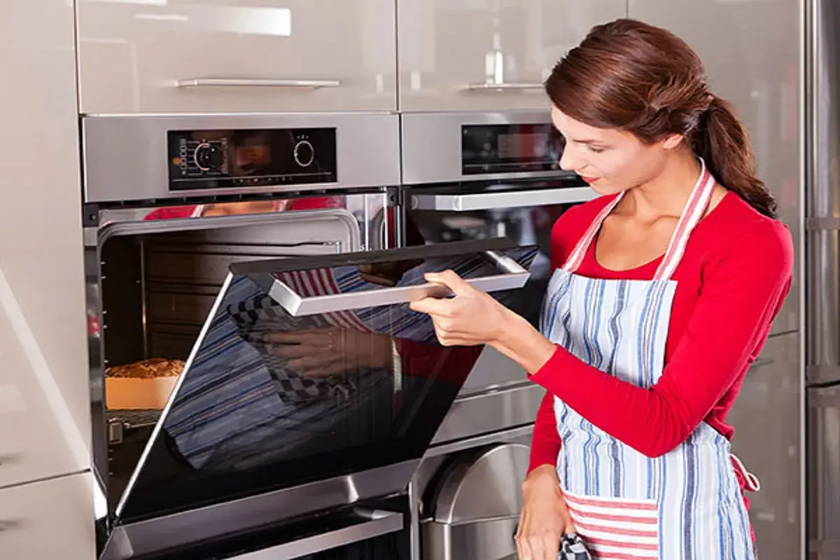 Mujer con delantal abre horno donde se hornea un pan.