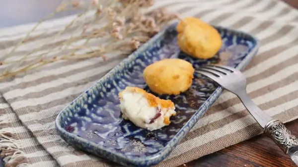 Croquetas de jamón doradas y cremosas en plato azul, una partida.