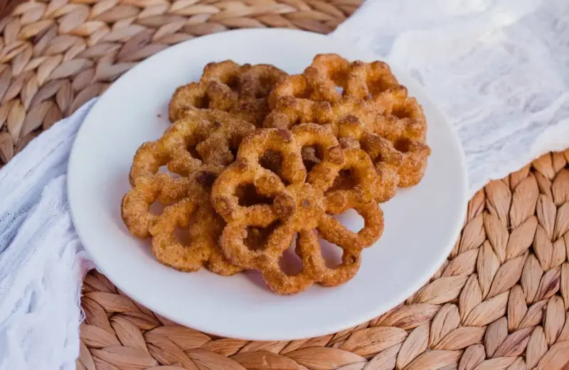 Buñuelos dorados con azúcar y canela en un plato blanco.