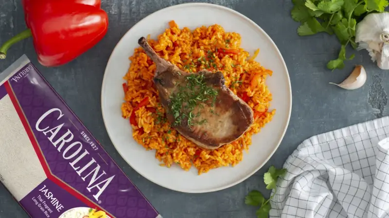 Chuleta de cerdo jugosa sobre arroz rojo con pimientos.