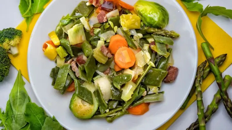 Menestra de verduras variadas con trozos de jamón en un plato blanco.