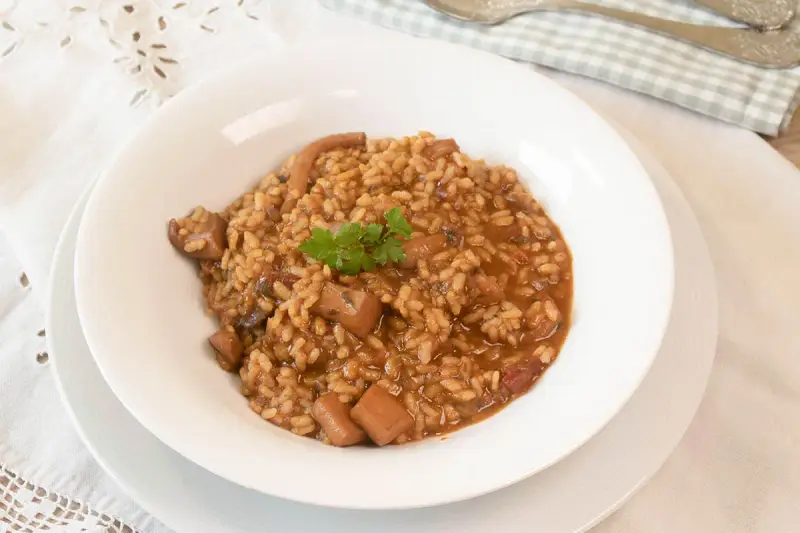 Arroz con sepia en un plato blanco, decorado con perejil.